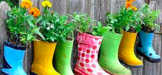 A picture of rainboots hung along a wooden fence with plants in them.