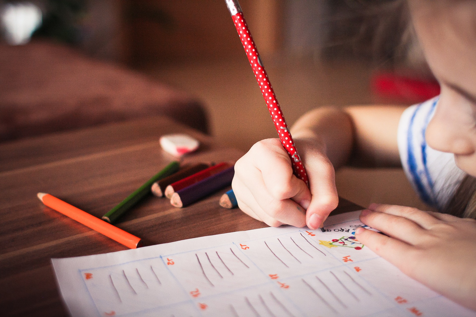 Child doing homework with a red pencil.