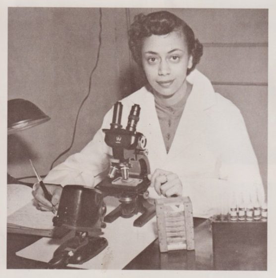 Sepia photograph of Dr. Jewel Plummer-Cobb. She is looking at the camera, sitting in front of a microscope.