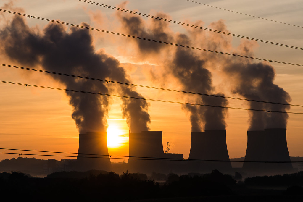 Power plants silhouetted against a sunset. They are towers spewing smog. 