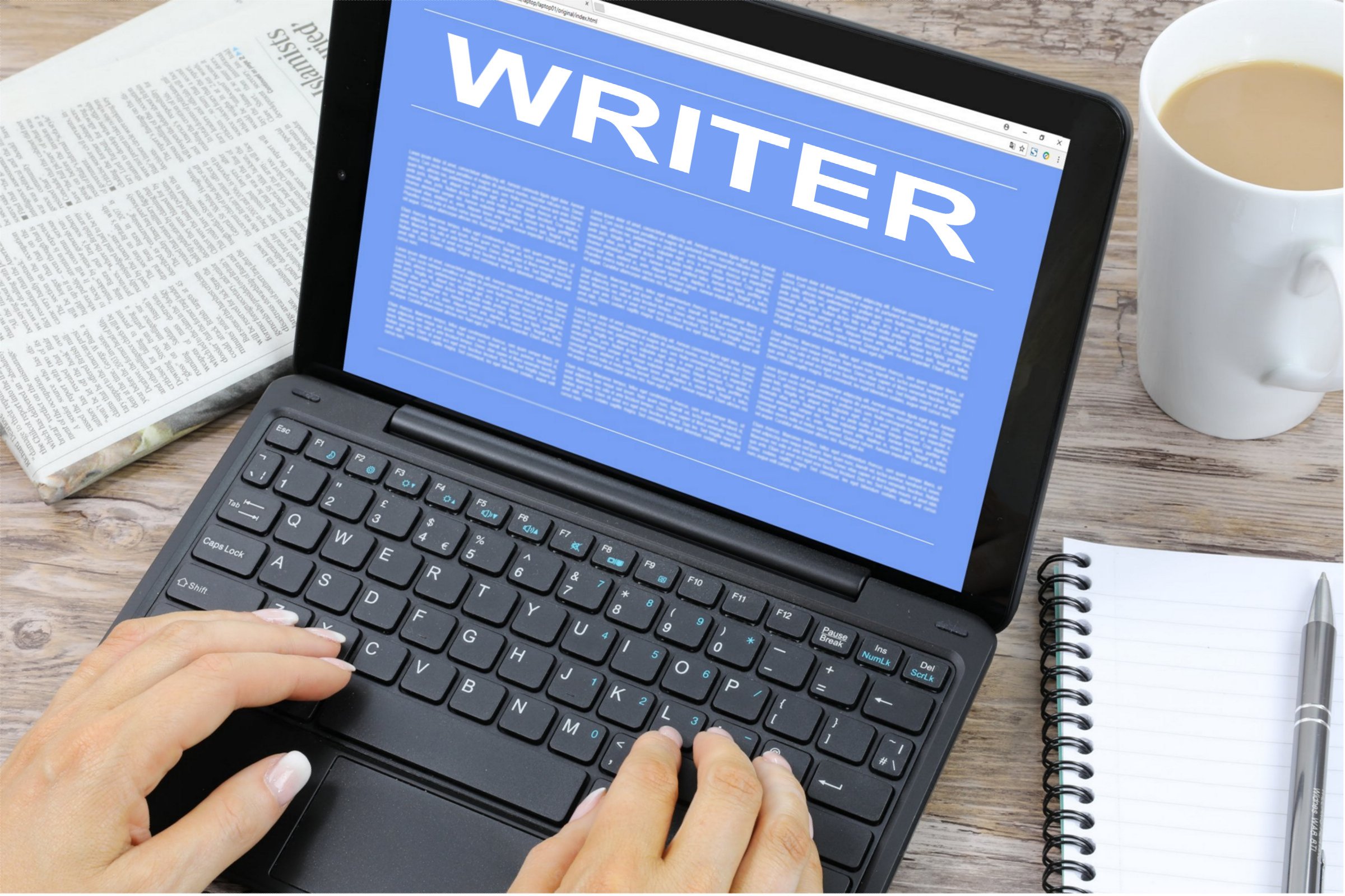 Black laptop with blue screen with white text saying "writer" in all capital letters. Hands hover over the keyboard.