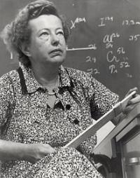 Black and white photograph of Dr. Maria Goeppert-Mayer in front of chalk board covered in math equations
