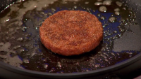 Cell-based hamburger patty on a frying pan, cooking. It looks like a meat patty.