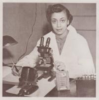 Sepia photograph of Dr. Jewel Plummer-Cobb. She is looking at the camera, sitting in front of a microscope.