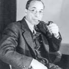 Black-and-white photograph of Dr. Elmer Imes. He is sitting in a chair, wearing a three-piece suit and tie and smoking a pipe.